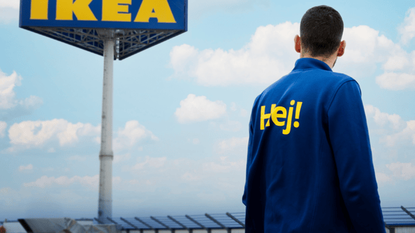 A co-worker stands in front of an IKEA sign, surrounded by solar panels under a clear sky.
