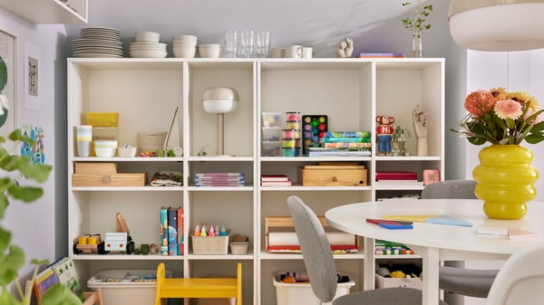 A VIHALS chair stands at a round VIHALS table in front of two white VIHALS shelving units in a small family dining room.