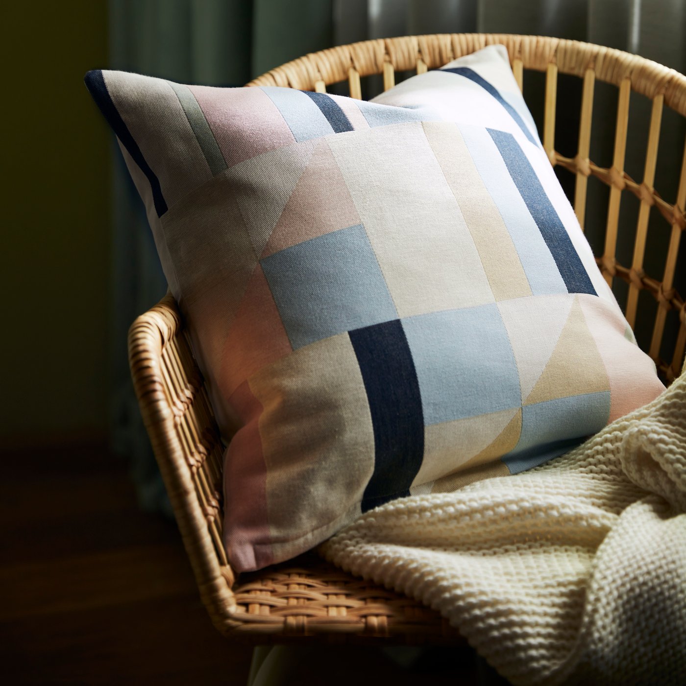 En LYKTBÄRARE kudde med geometriskt mönster ligger i en NILSOVE rottingstol.