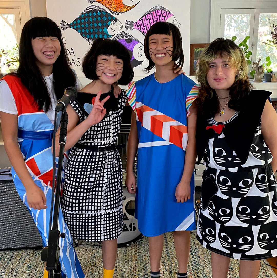 الفنانون أعضاء ‪The Linda Lindas‬ يرتدون ملابس ملونة أمام ميكروفون. 