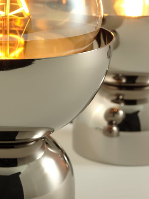 Close-up of two lit nickel-plated ACKJA table lamps, placed on a table.