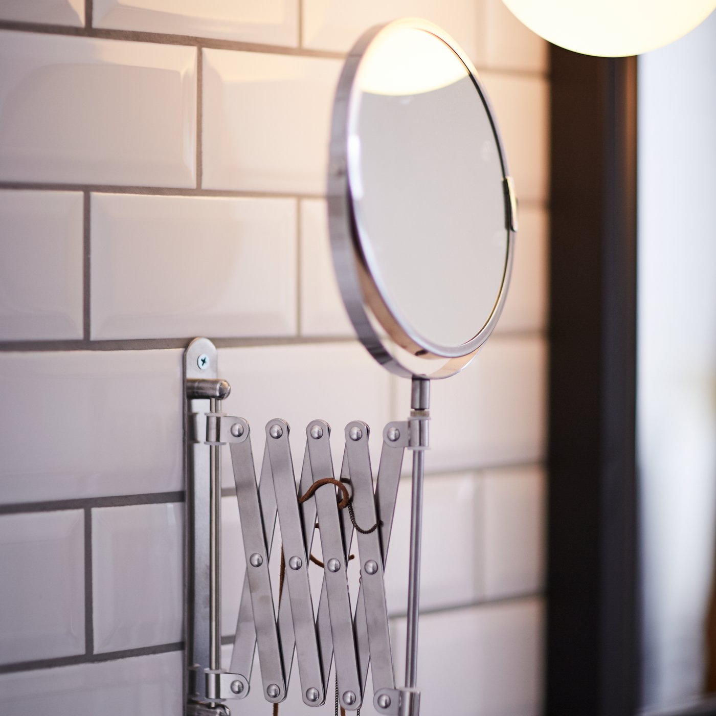 A FRÄCK stainless steel mirror against a white tiled bathroom wall.