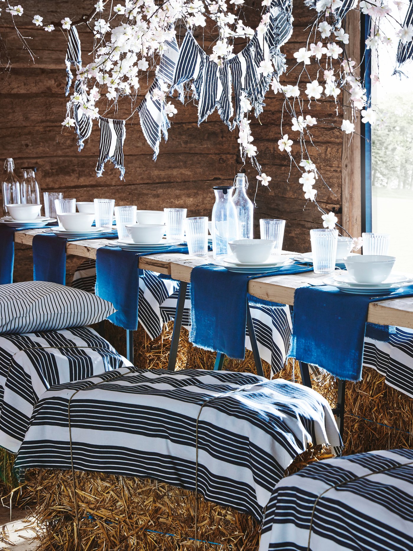 حظيرة قديمة جاهزة لحفلة مع طاولات وزينة معلقة وبالات قش مغطاة بقماش METTALISE لون أبيض/رمادي داكن.