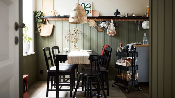 A black stained pine HÄGERNÄS table and 4 chairs and a black AGAM junior chair stand in a small cottage-style dining area.