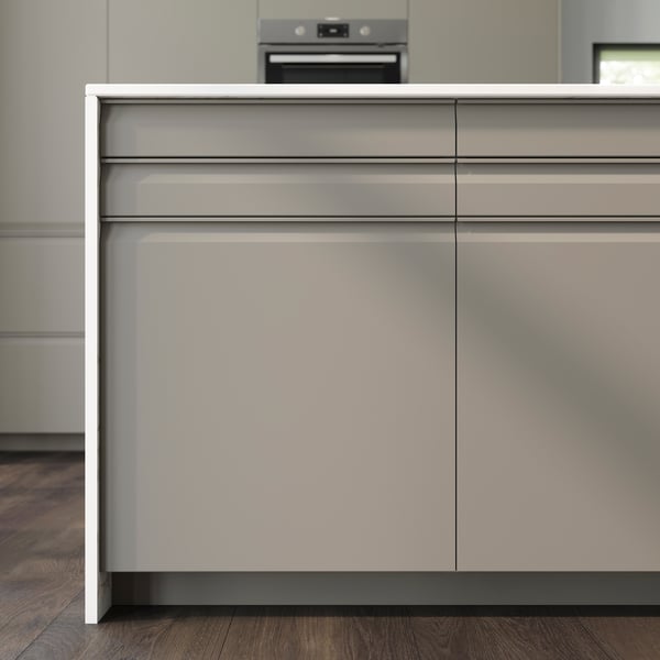 Køkkenskabe med UPPLÖV køkkenfronter i mørk beige med integrerede greb og en hvid bordplade med vandfaldseffekt ovenpå. En ovn kan anes i baggrunden.  