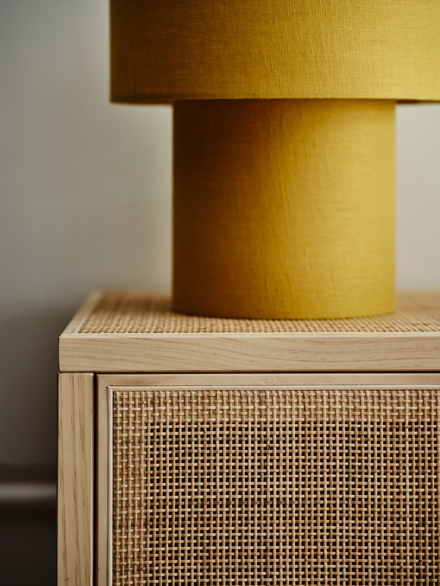 Close-up of a yellow cylindrical lampshade on a light wooden cabinet with woven rattan detailing.