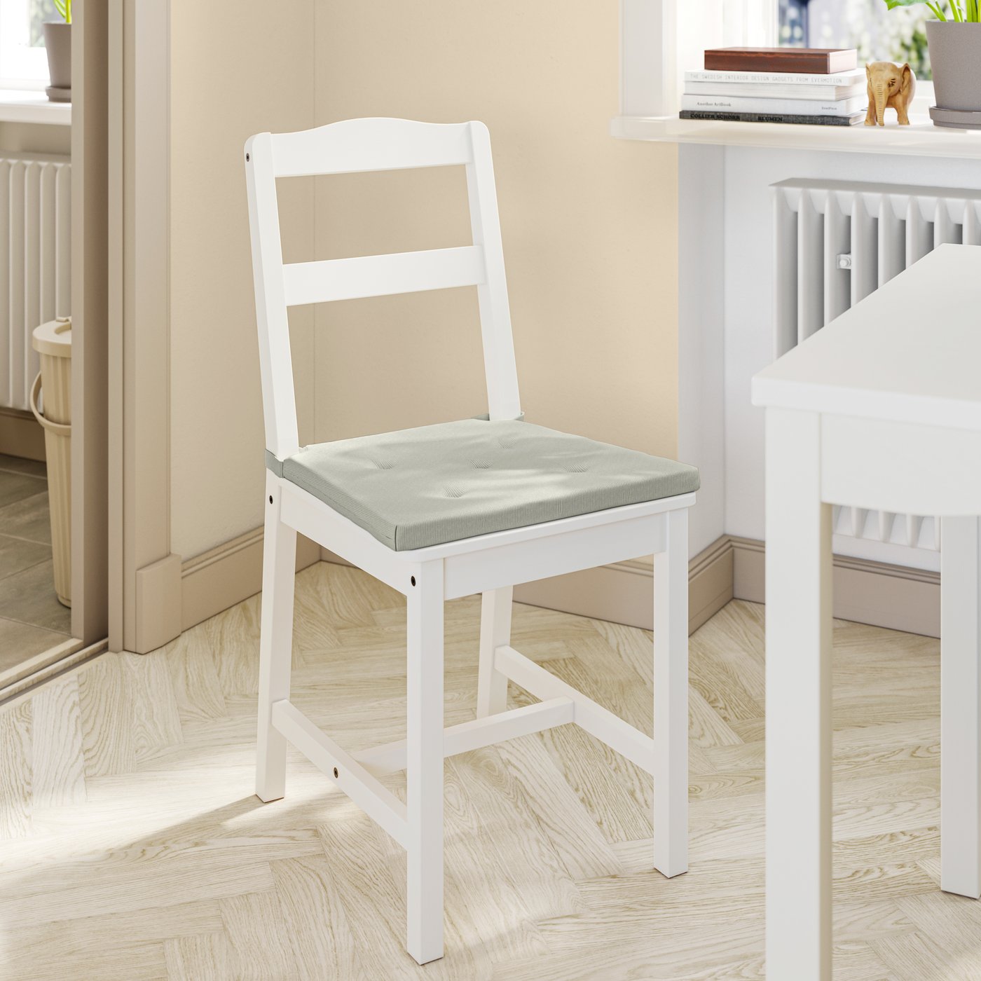 A white dining chair with a light green JUSTINA chair cushion on it for extra seating comfort.