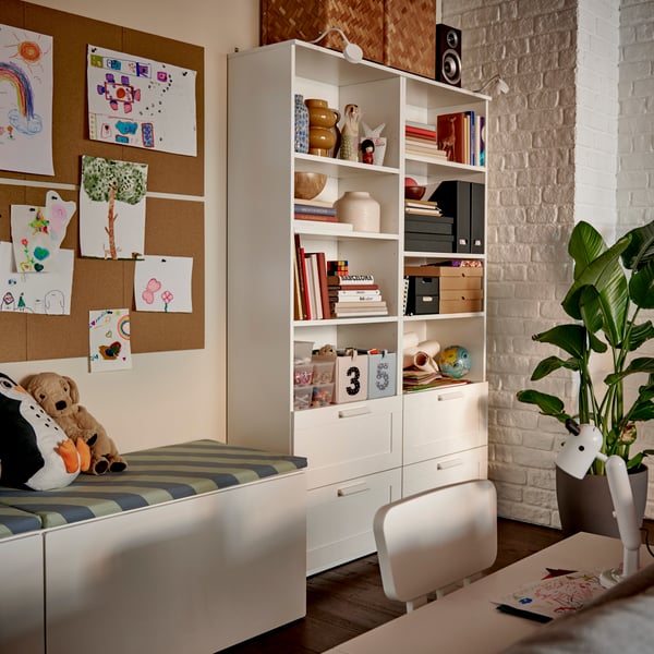 A white BRIMNES bookcase filled with books and decorative boxes, beside a cosy reading nook with soft-toy animals.