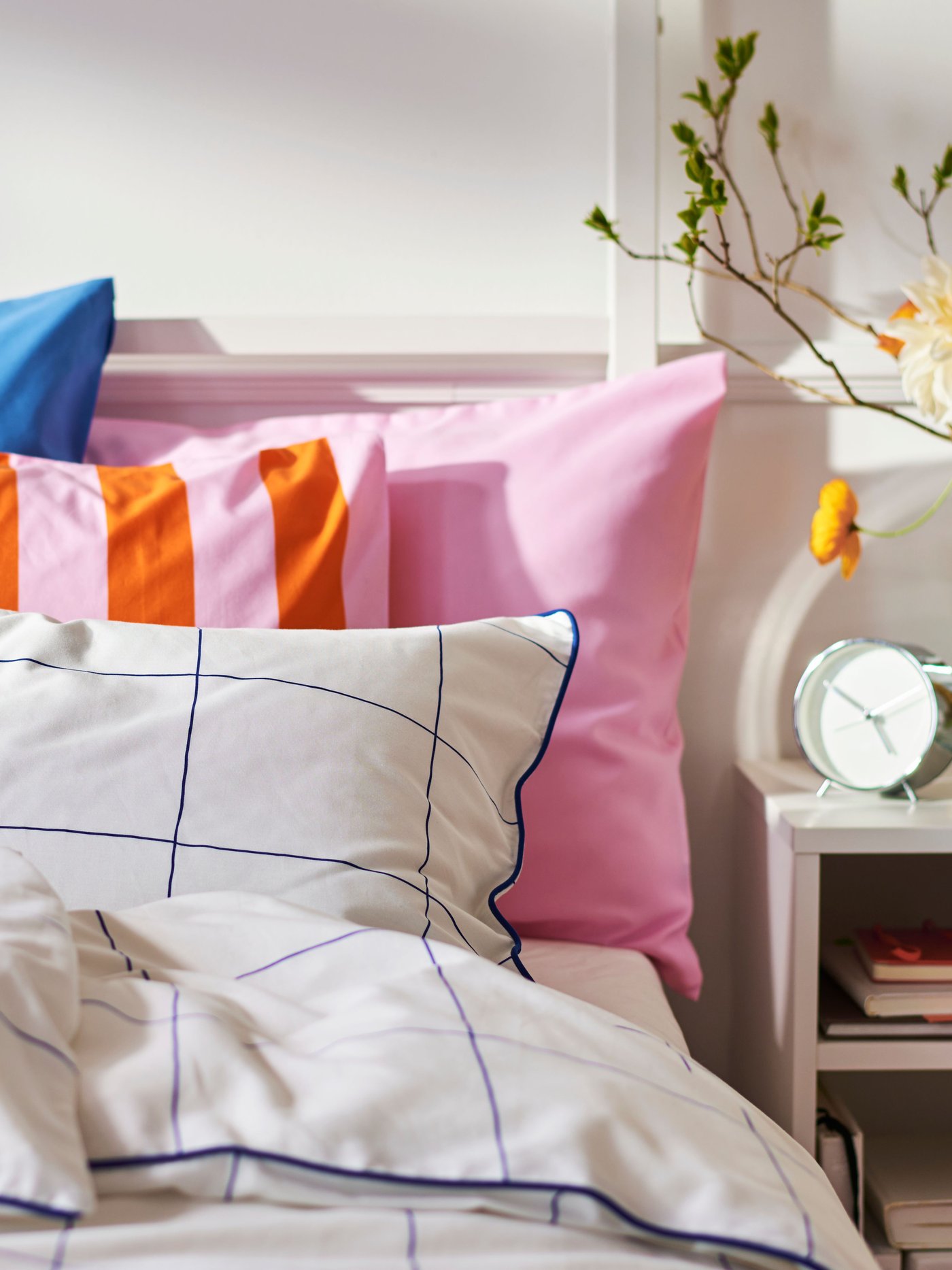 Close-up of bed with a lot of pillows in different patterns and colours. Bedside table on the right.