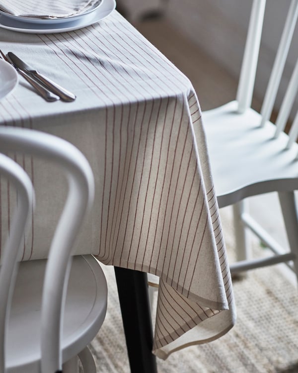 A VIPPSTARR tablecloth with a red/natural striped pattern draped over a black dining table, surrounded by white dining chairs.