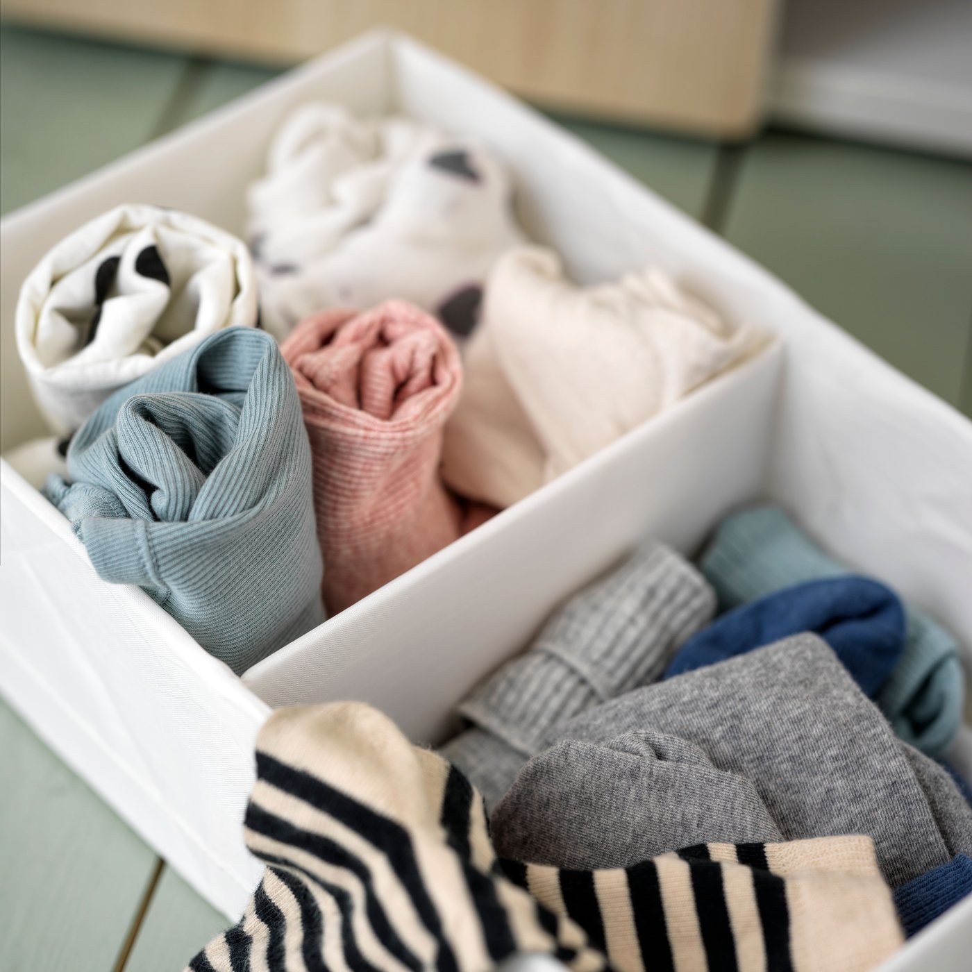 A white STUK box with compartments on a green floor holding different types of rolled clothing and coloured socks.