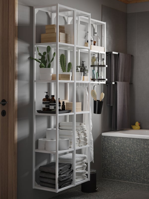 A white ENHET high frame with shelves has grey and white towels, toilet paper rolls and bathroom products on the shelves.
