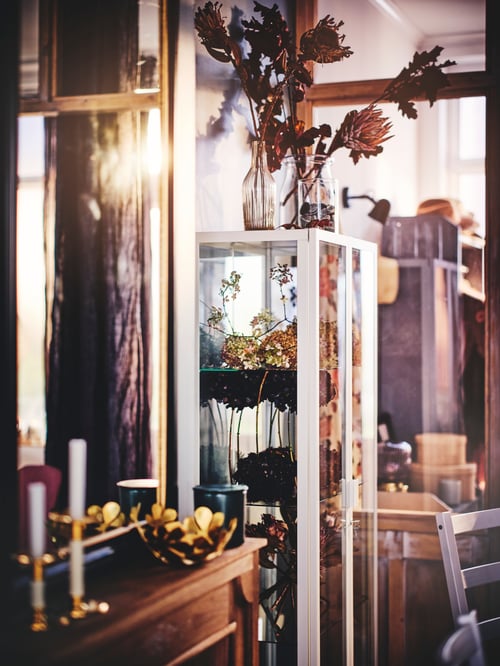A modern living room that features a glass door cabinet, a yellow bowl, and a set of three glass vases.