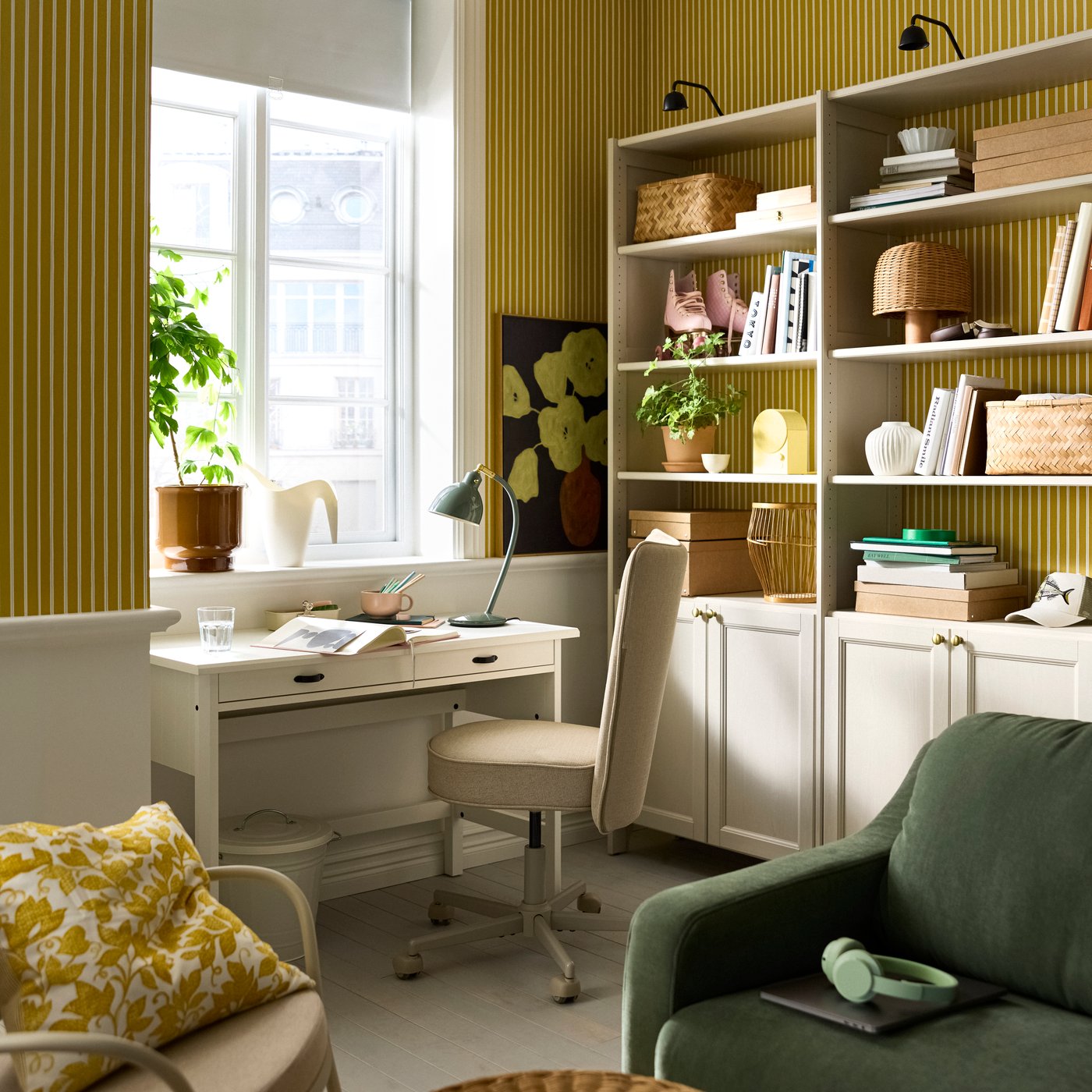 A living room with a beige GULDDRAGARE storage combination, with cabinets and shelves, beside a BRYTNING desk and chair.