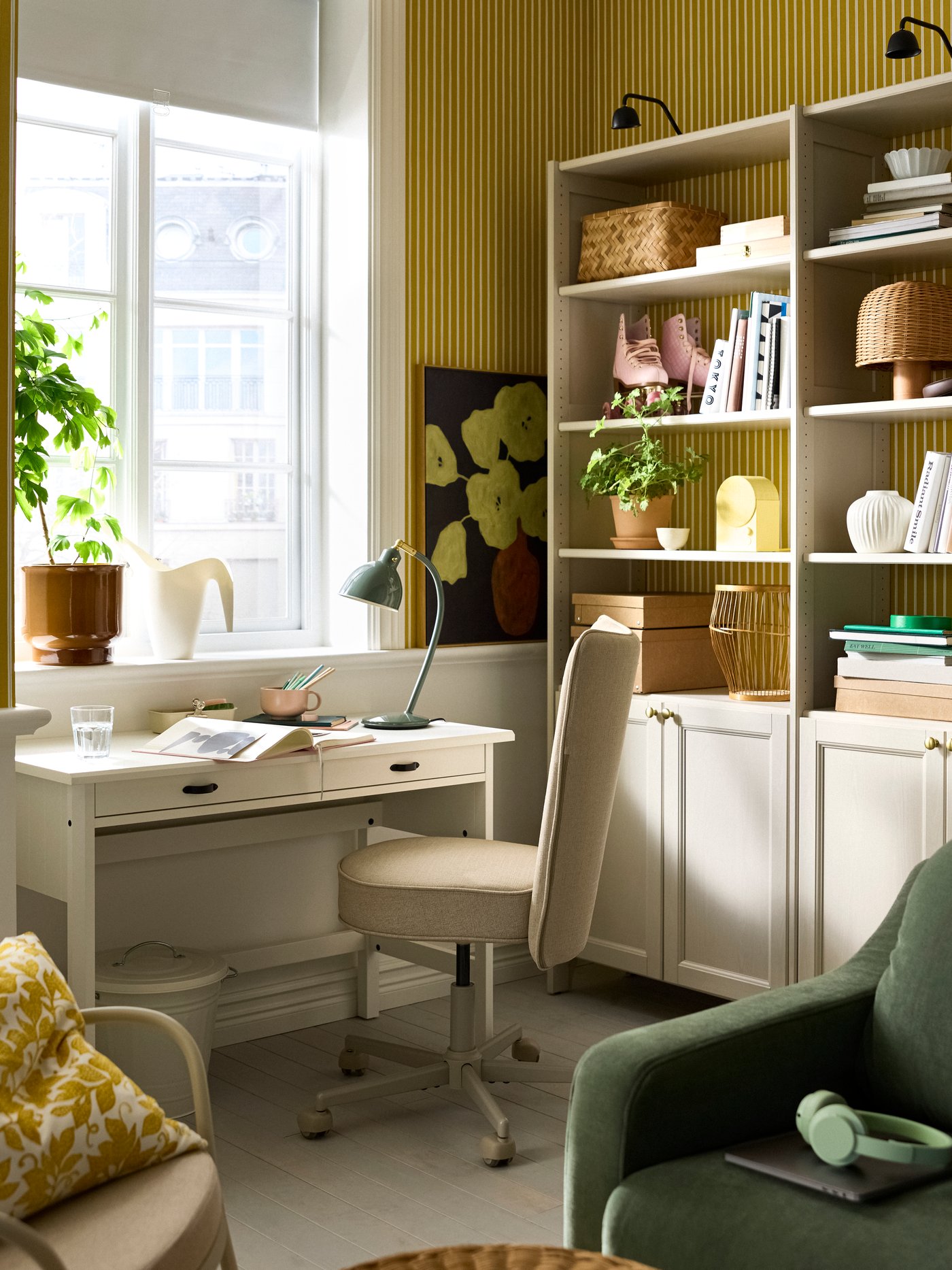 A living room with a beige GULDDRAGARE storage combination, with cabinets and shelves, beside a BRYTNING desk and chair.