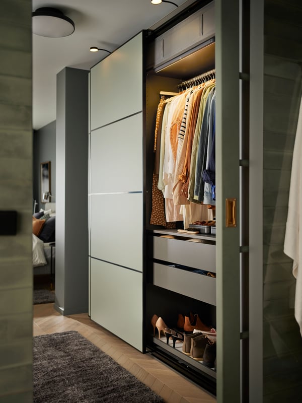 A PAX wardrobe combination in green with one door open to show hanging clothes in perfect order.