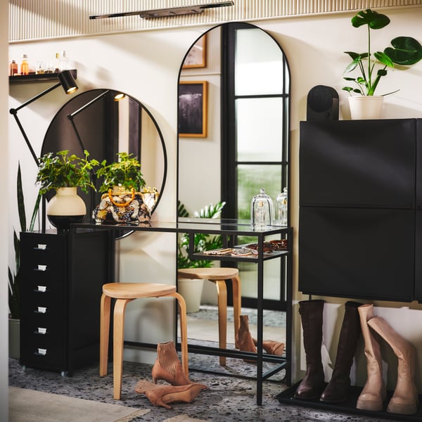 Modern sminkstation med svarta möbler, gröna växter, rund spegel med lampor på sidorna och träpallar