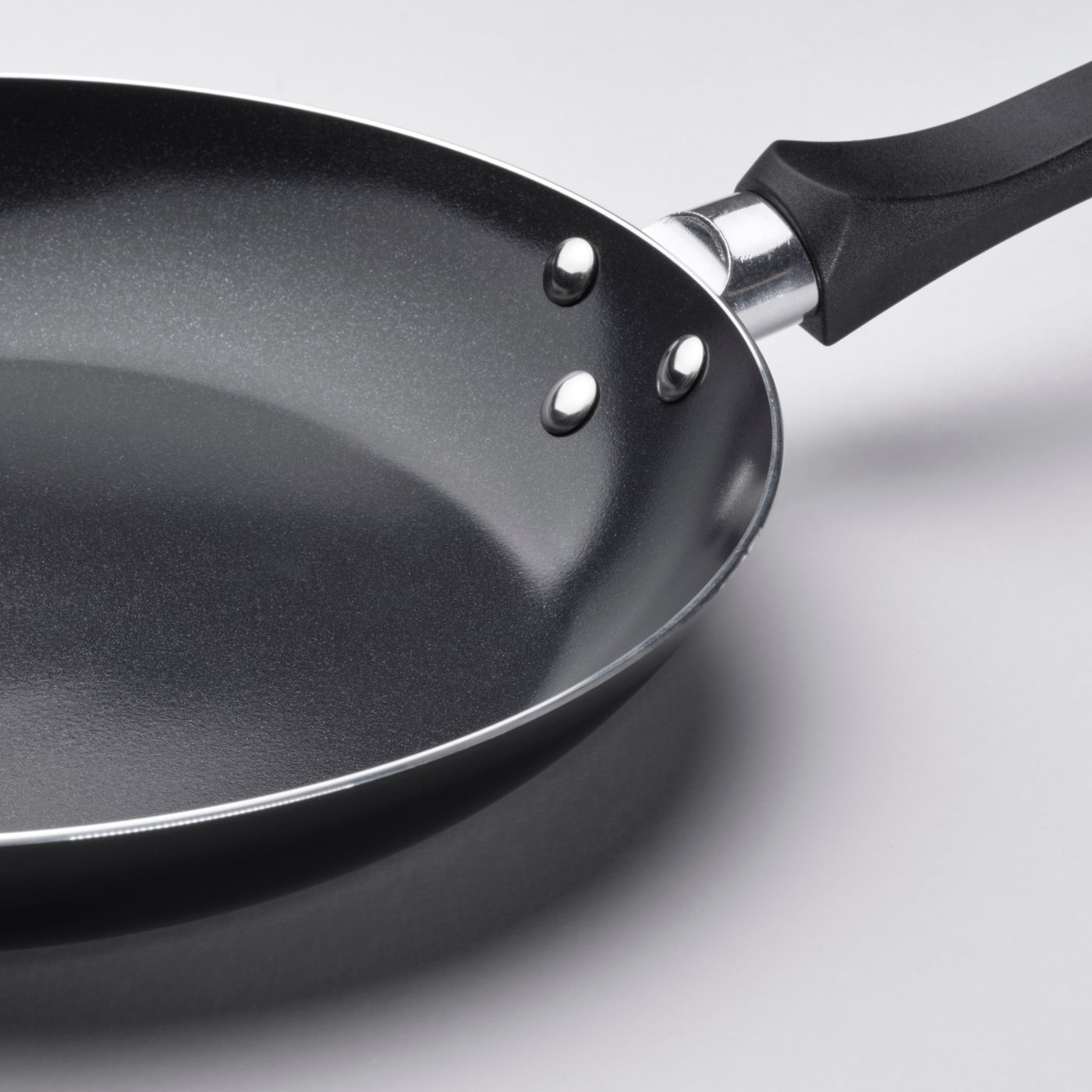 A close-up of a 24-cm TAGGHAJ black non-stick frying pan, emphasising where the easy grip handle is attached.