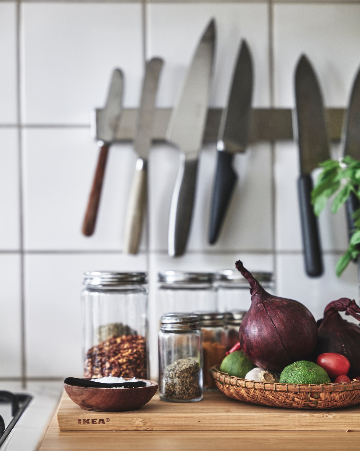 Ett knivställ hänger på en vägg, framför står en skärbräda med diverse grönsaker och kryddburkar.