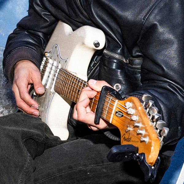 Primo piano di mani che suonano una chitarra elettrica bianca, con giacca in pelle nera: un momento di musica dal vivo che accende l’atmosfera e invita a fermarsi ad ascoltare.