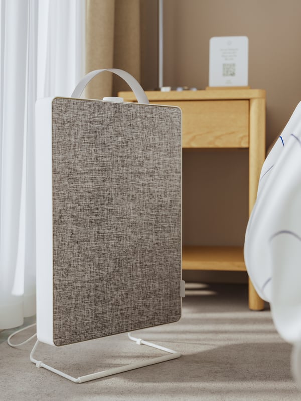 A white FÖRNUFTIG air purifier stands on the floor next to a TONSTAD bedside table in oak veneer in a hotel room.