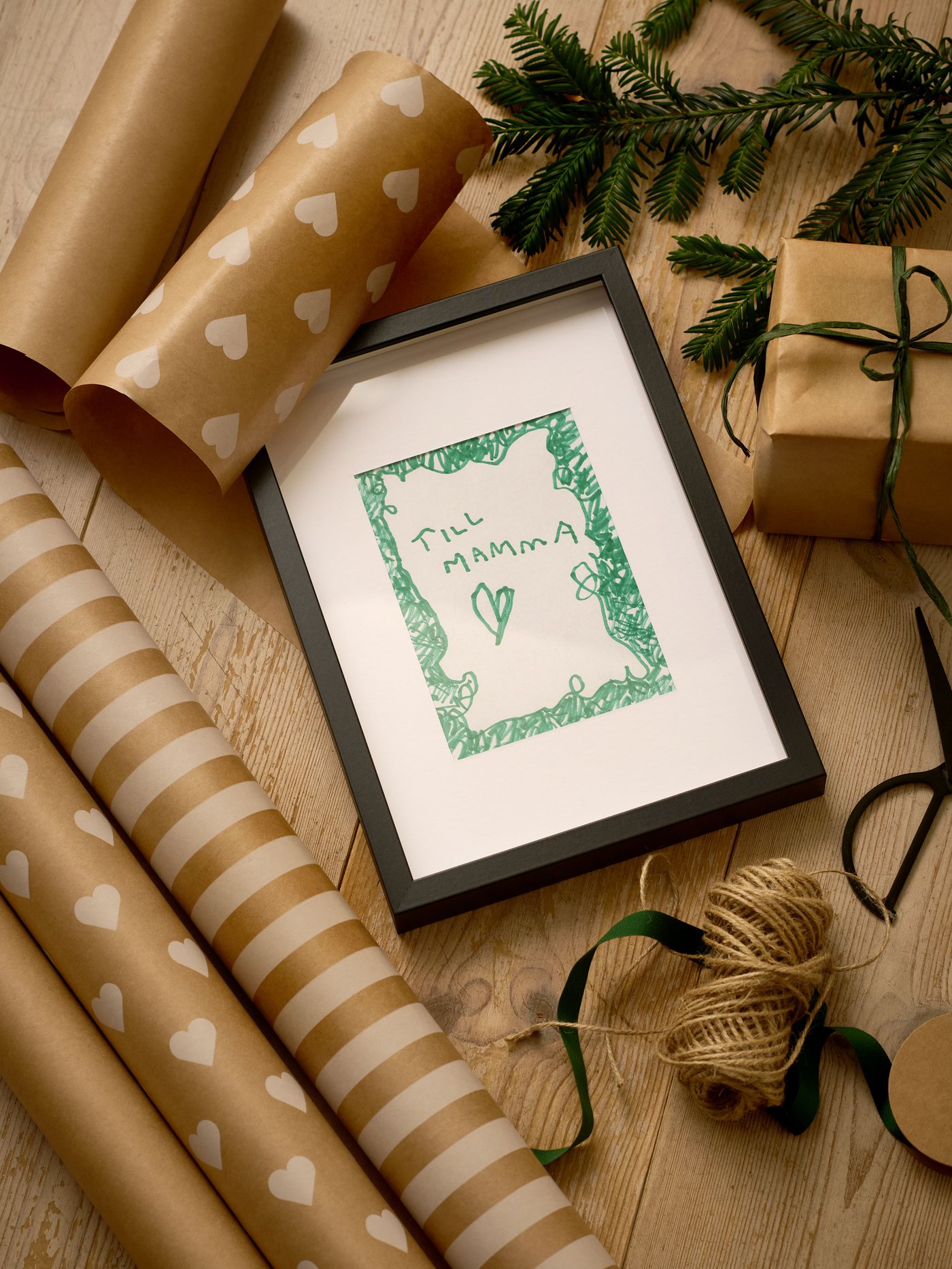 Svart tavelram omgivet av presentpapper, grankvistar och julsnöre.