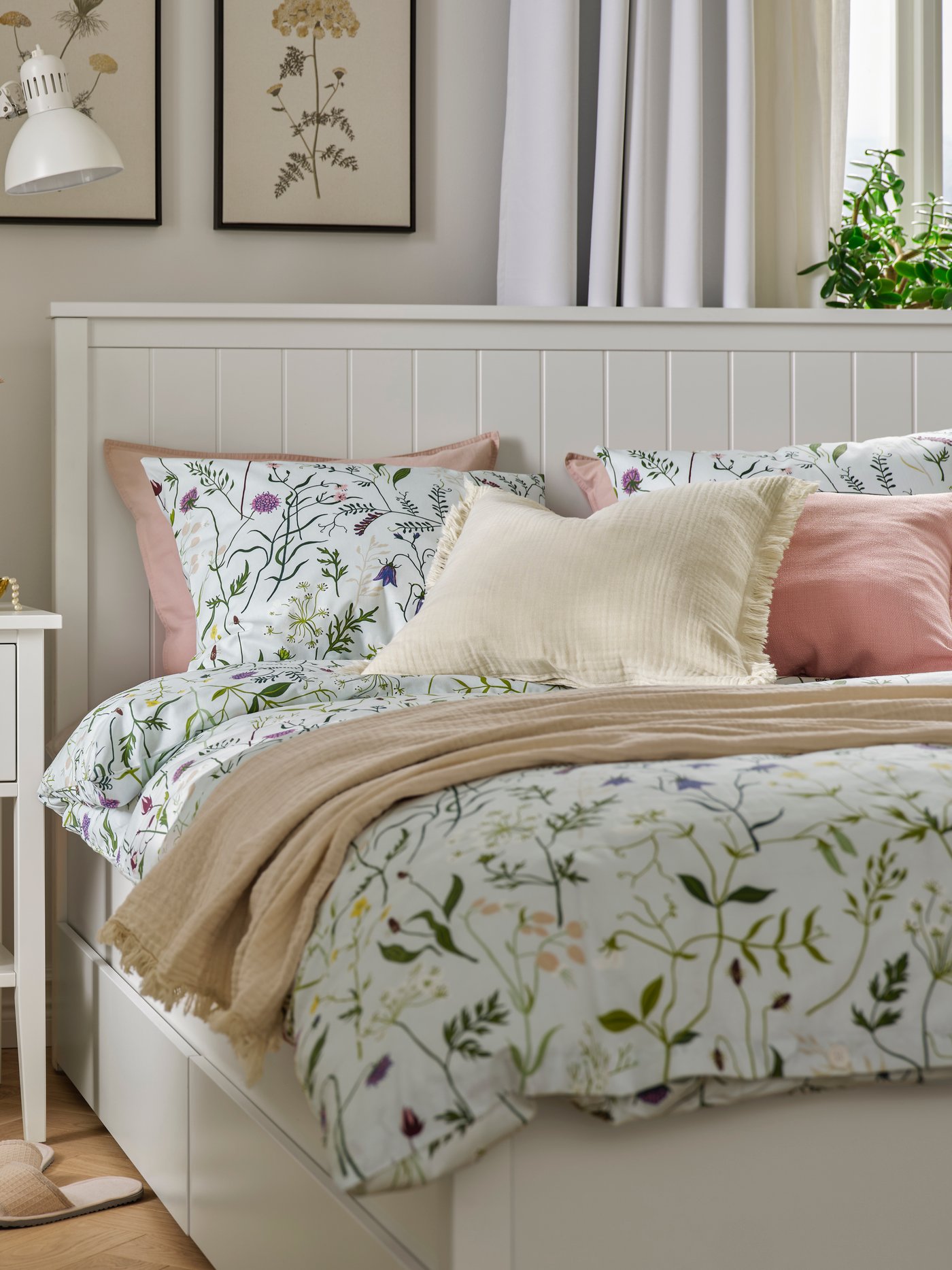 Camera da letto accogliente con struttura letto e comodino GULLABERG, biancheria da letto MATTOXBÄR a motivi floreali, cuscini e coperta decorativa.