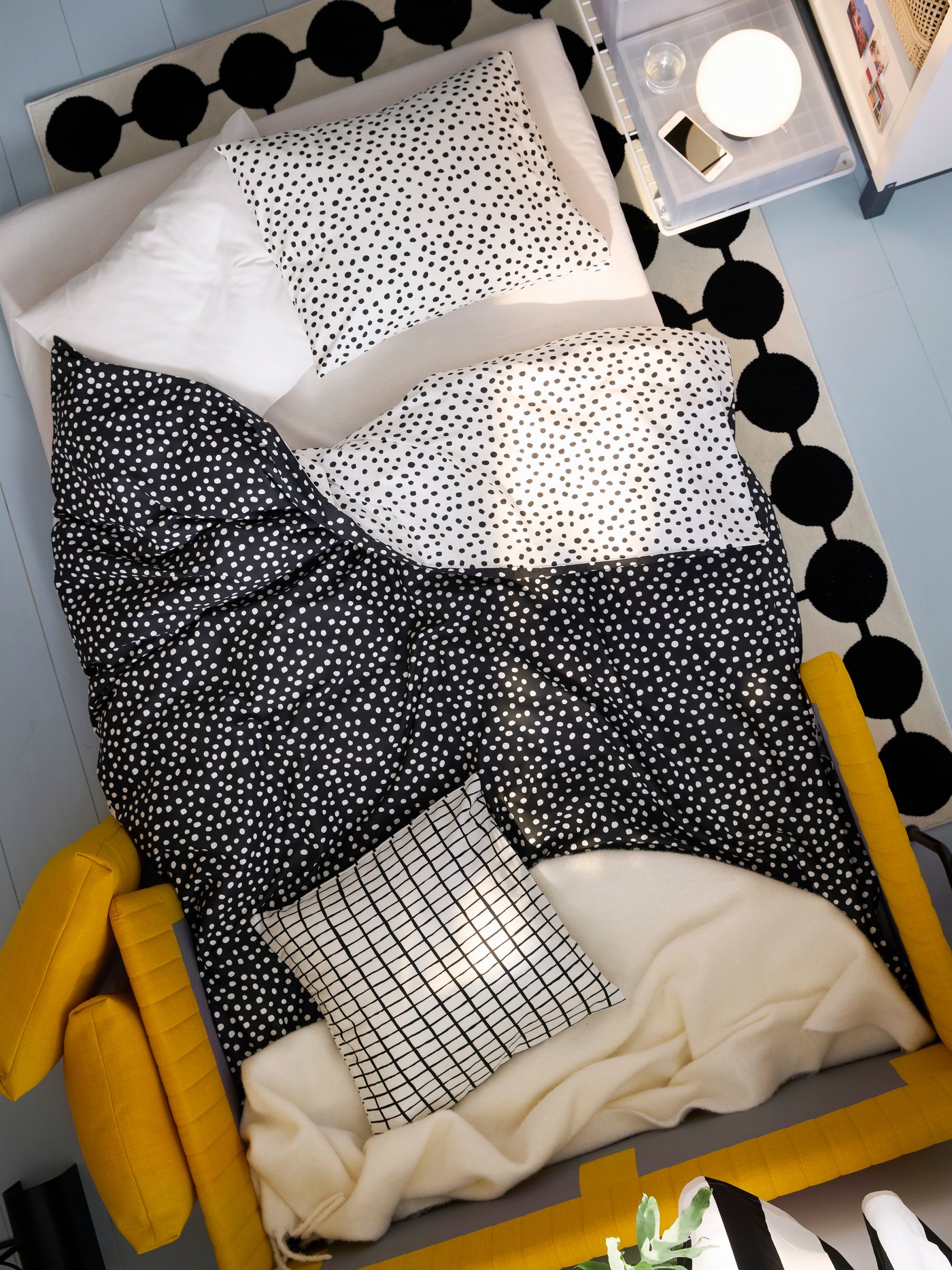 A FRIDHULT sofa-bed, configured as a bed, with BJÖRKGRÅMAL bed linen and an off-white KLIPPOXEL throw, stands on a rug.