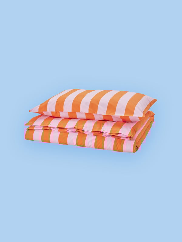 Es sind ein Kissen und eine Decke in Orange und Rosa vor einem blauen Hintergrund zu sehen.