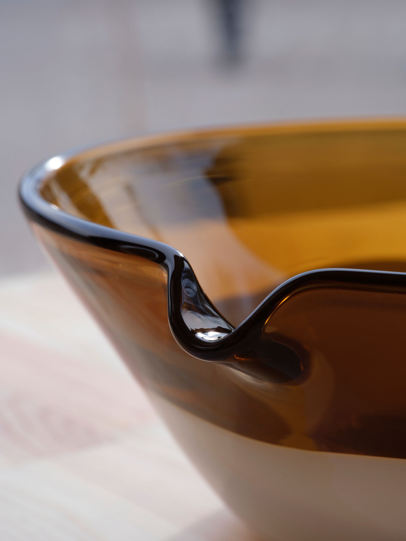 A close-up of the spout of a brown/white OMMJÄNGE serving bowl made of glass. The shades of the glass shift in the light.