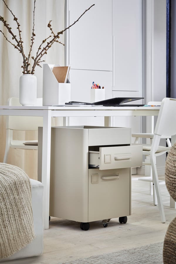 Ved siden af en seng står et hvidt bord med arbejdsrelateret tilbehør og et IDÅSEN skuffeelement under det.