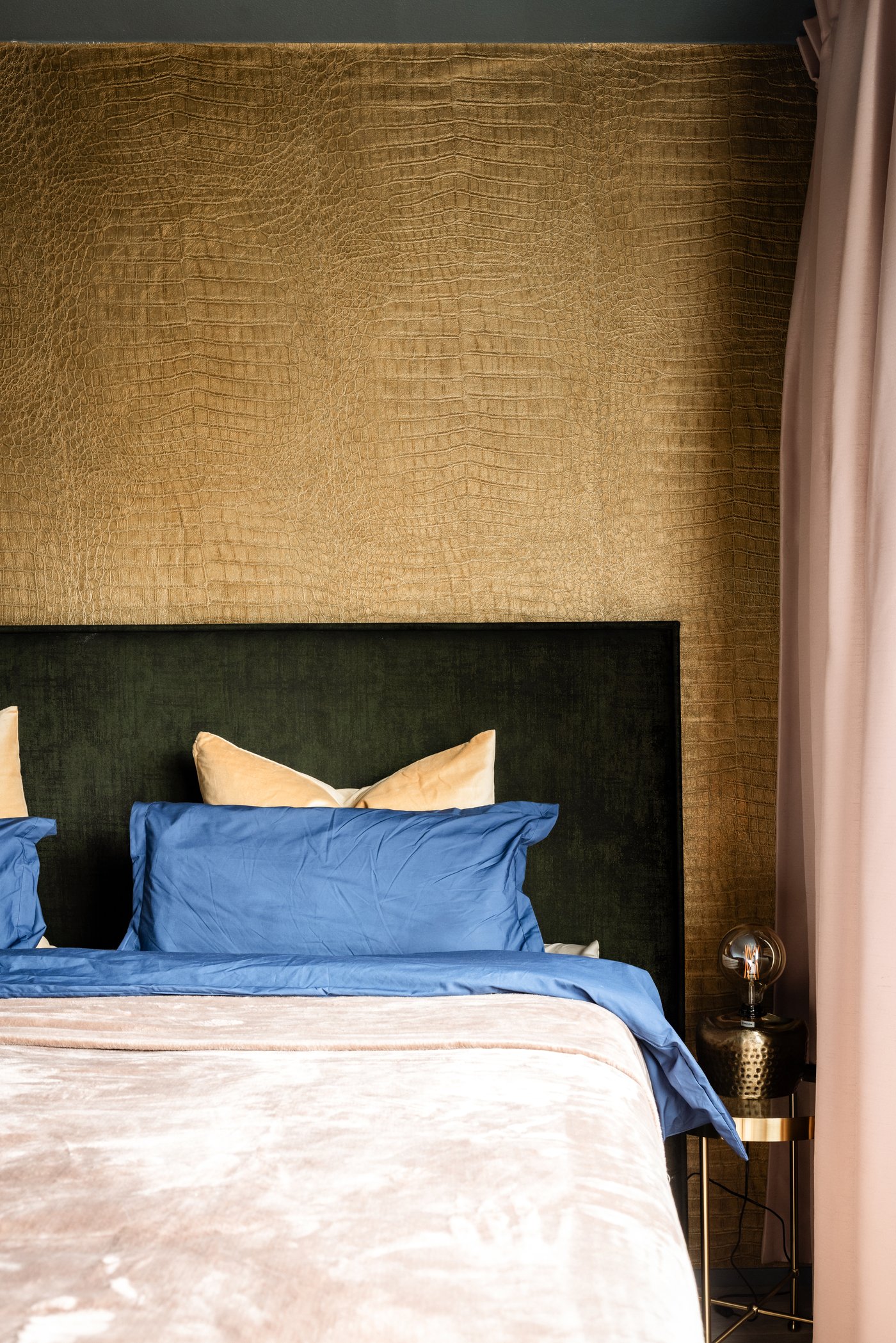 Hoek van een bed met daarnaast een gouden TORSJÖ tafeltje met daarop een lamp.
