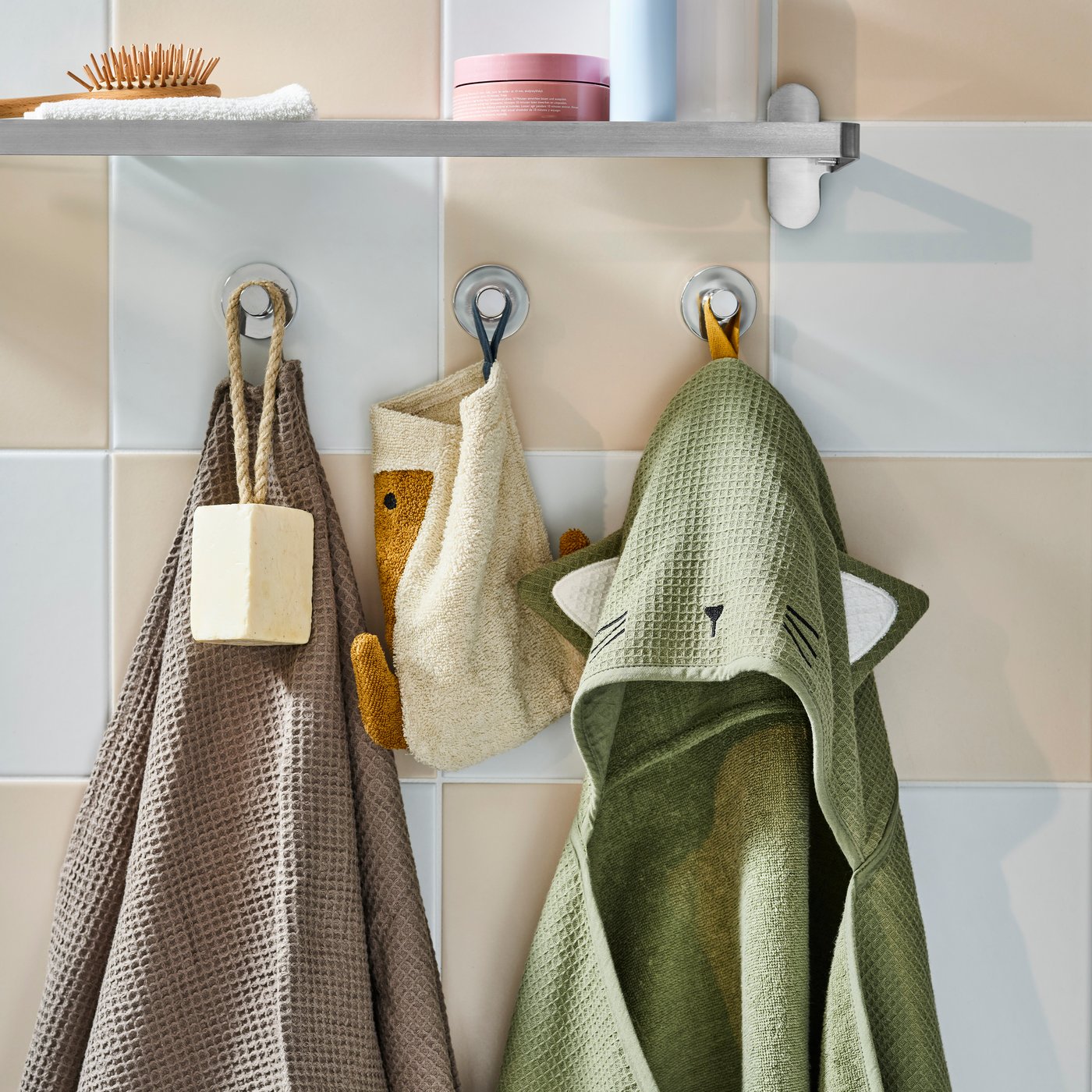 Dettaglio di un bagno dove c'è appeso l'accappatoio per neonato GULDVÄVARE di color verde con cappuccio a orecchie e musetto ricamato.