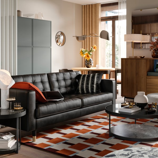 A three-seat leather and coated fabric sofa in a living room near several BESTÅ storage solutions and a RÅDMANSJÖ cabinet.