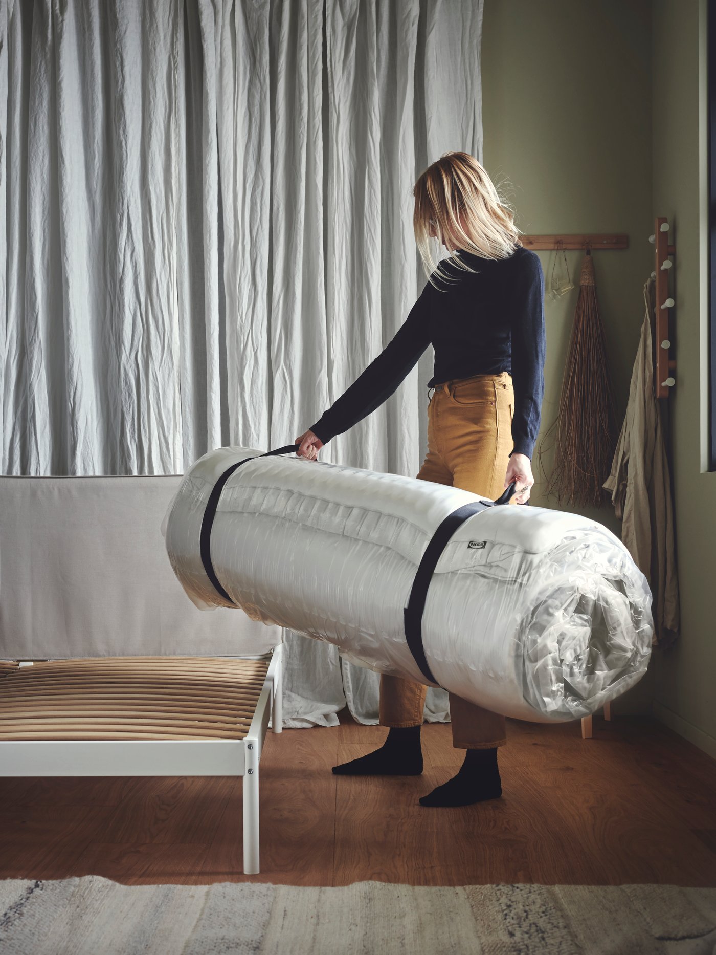 Een persoon plaatst een opgerolde tapijtrol op een houten bankje in een rustige, modern ingerichte kamer.