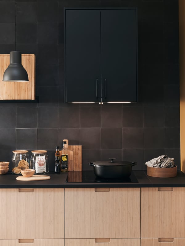 A kitchen cooking area with METOD cabinets, a black HEKTAR lamp and an induction cooktop.