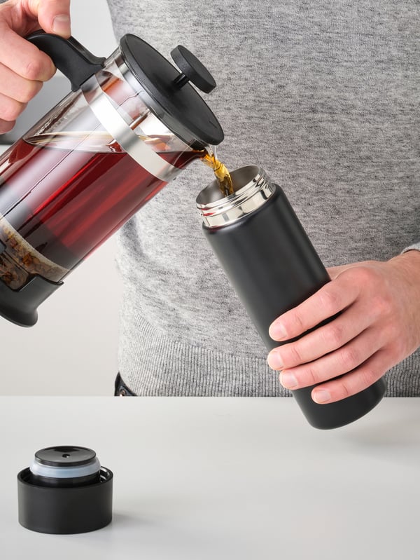 Hands pouring hot coffee into a steel vacuum flask.