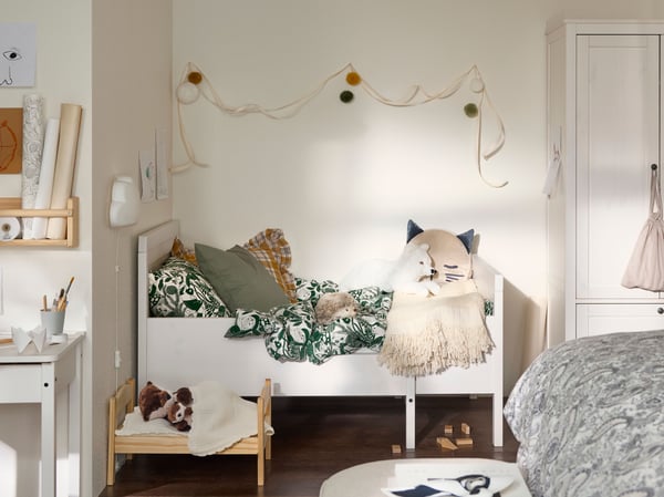 A child’s corner of the bigger bedroom, with SUNDVIK extendable bed, pillows, toys and paper decorations on the wall.  