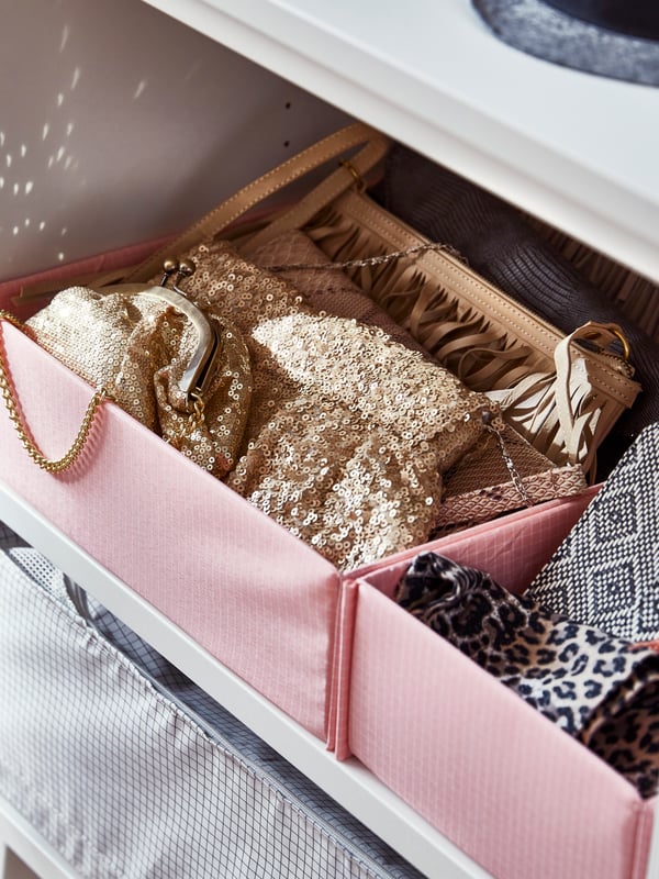 Caixas com compartimentos STUK em rosa, com malas pequenas, carteiras e lenços, numa prateleira dentro de um roupeiro.