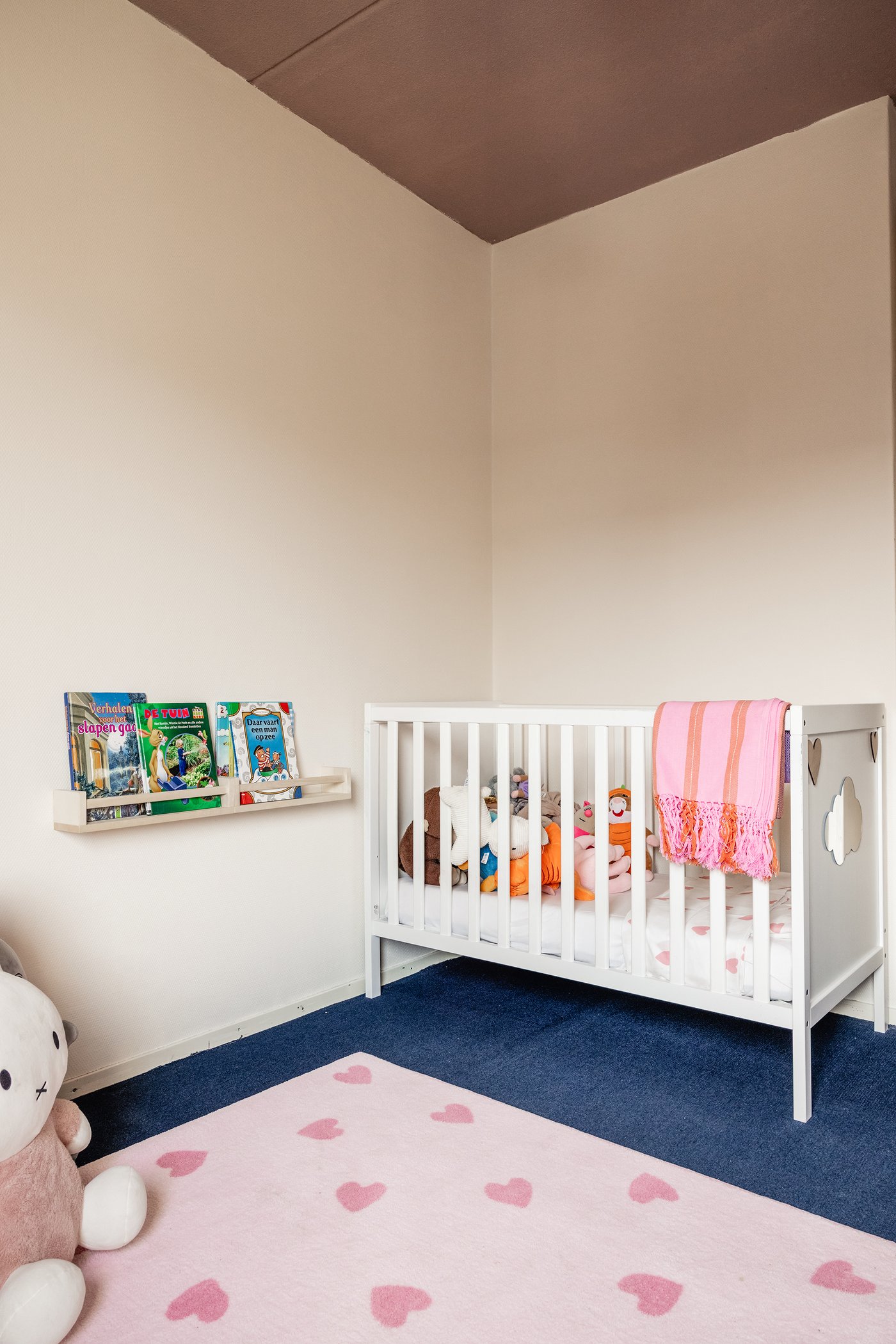 In de hoek van een kinderkamer staat een wit SUNDVIK babybed. Op de grond ligt een roze BARNDRÖM vloerkleed met hartjespatroon.