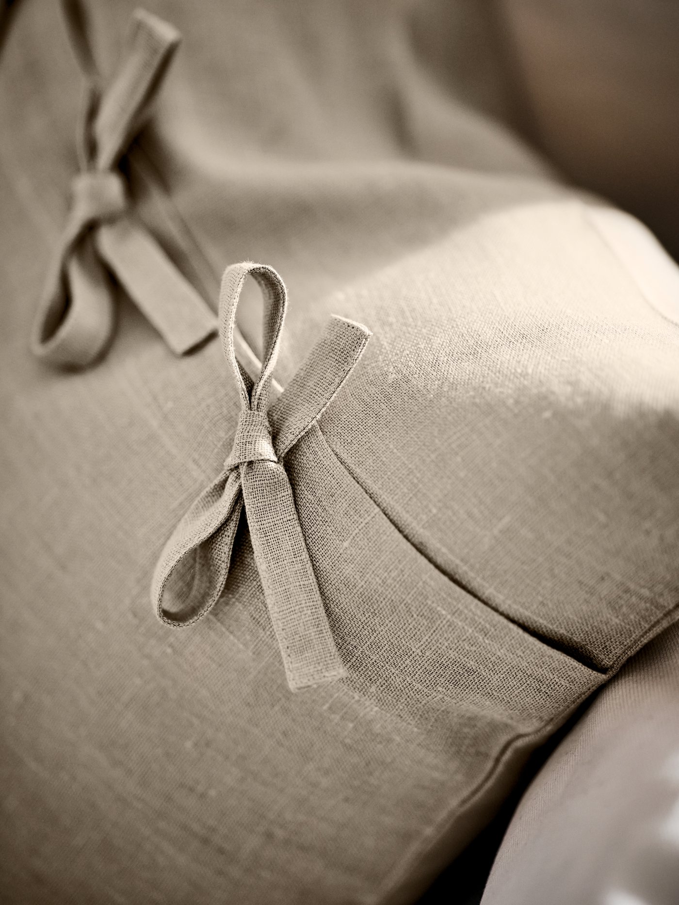 L’arrière d’un coussin AINA beige sur un canapé couleur crème, montrant deux des attaches nouées.