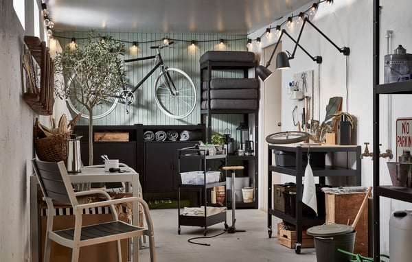 Garagelignende rum med en cykel hængt op på væggen, reoler med udendørsting, en stol, kaffe, stemningsbelysning og funktionel belysning.