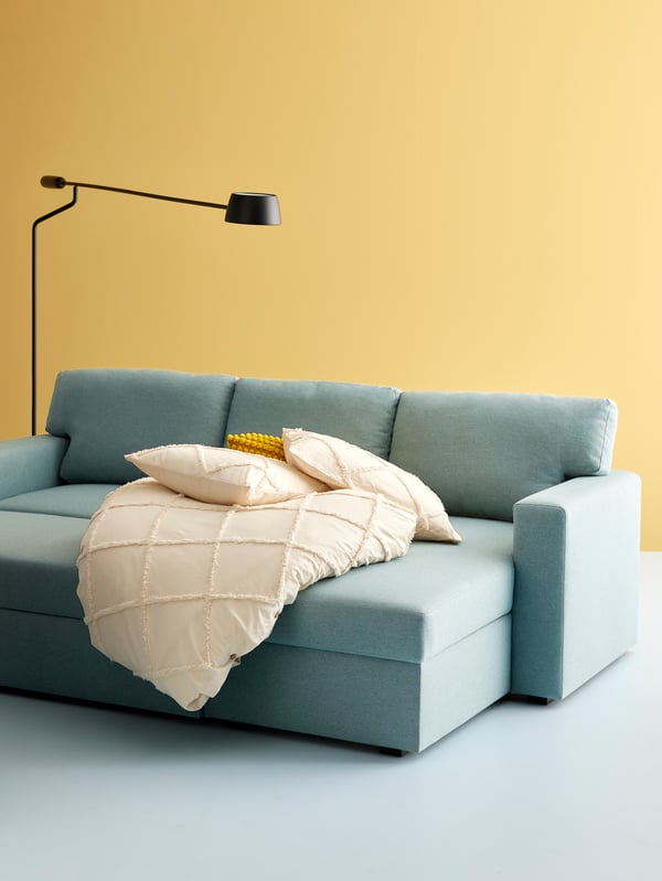 A VÅGHÖJD LED floor lamp is hovering over a BÅRSLÖV sofa bed with chaise lounge in a space with mustard-coloured walls.