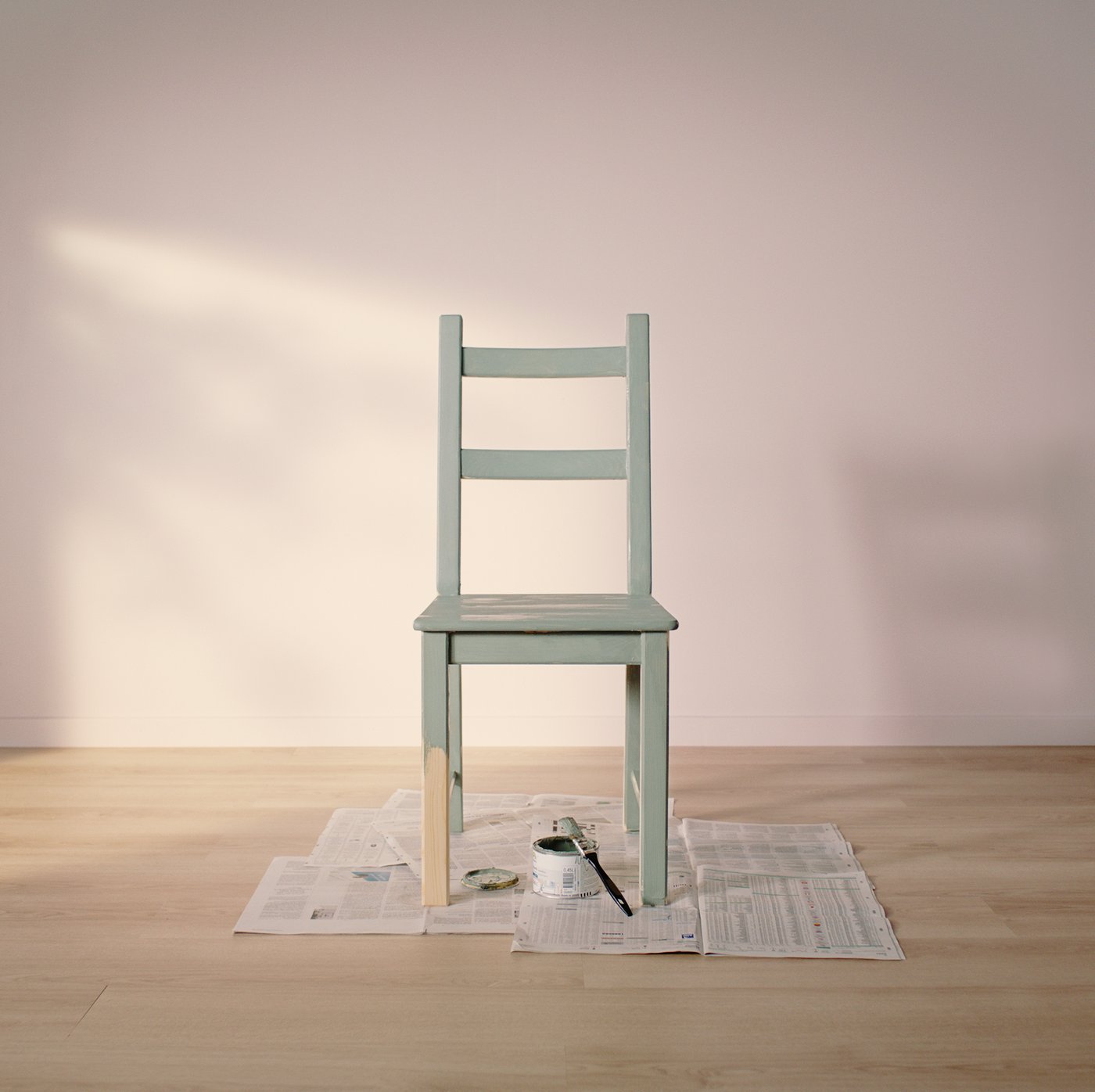 Ein grün gestrichener IVAR Stuhl steht in einem leeren Zimmer mit einem hellen Holzboden und Wänden in Hellrosa auf alten Zeitungen.