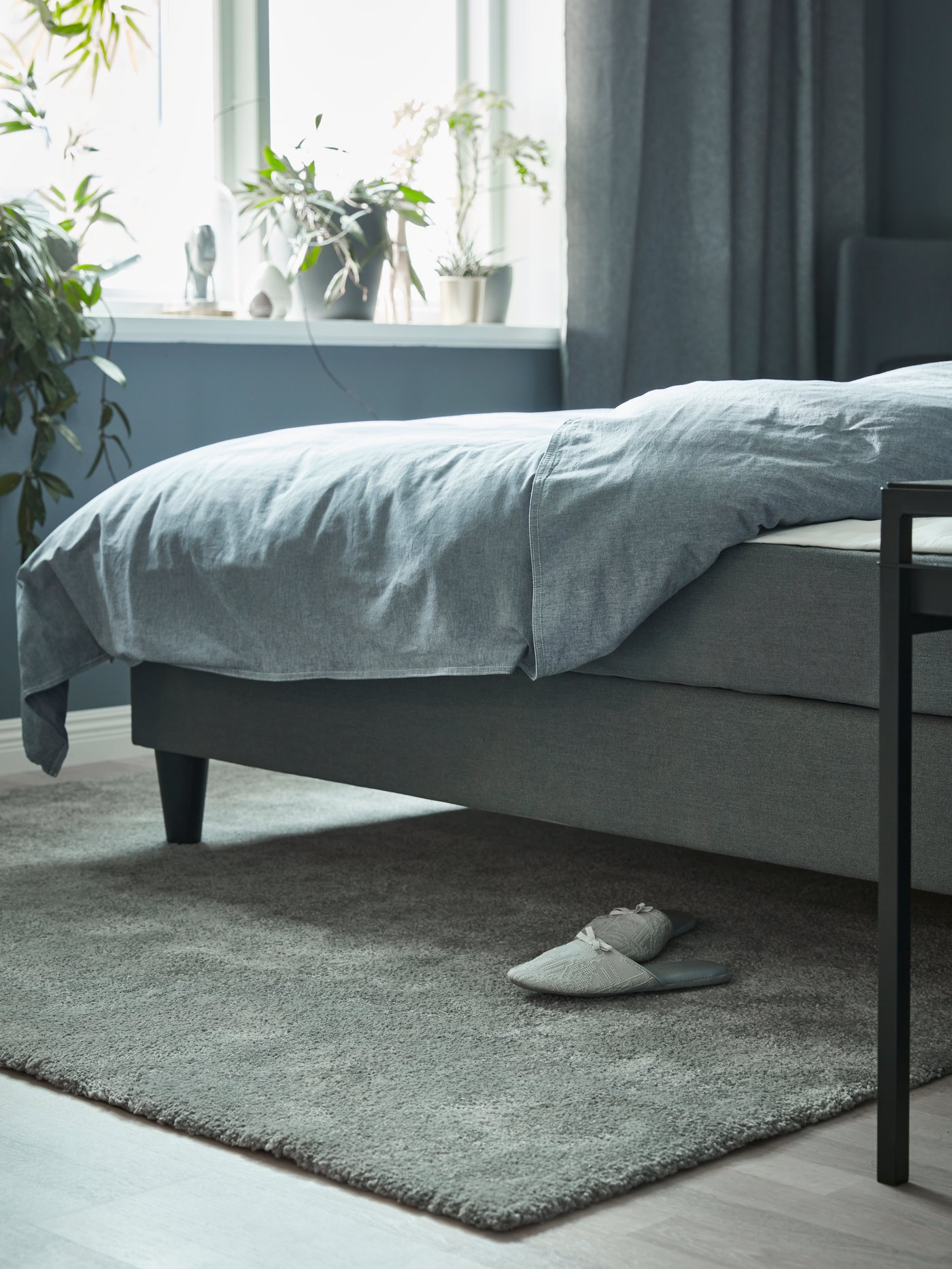 Dormitorio con una alfombra rectangular de pelo corto hecha de polipropileno colocada bajo un diván cama cubierto con una funda nórdica azul. 