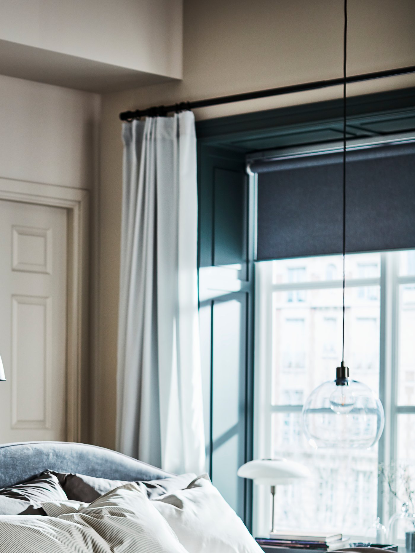 Una camera da letto illuminata dalla luce proveniente da un'ampia finestra con un bastone per tenda nero BEKRÄFTA. 