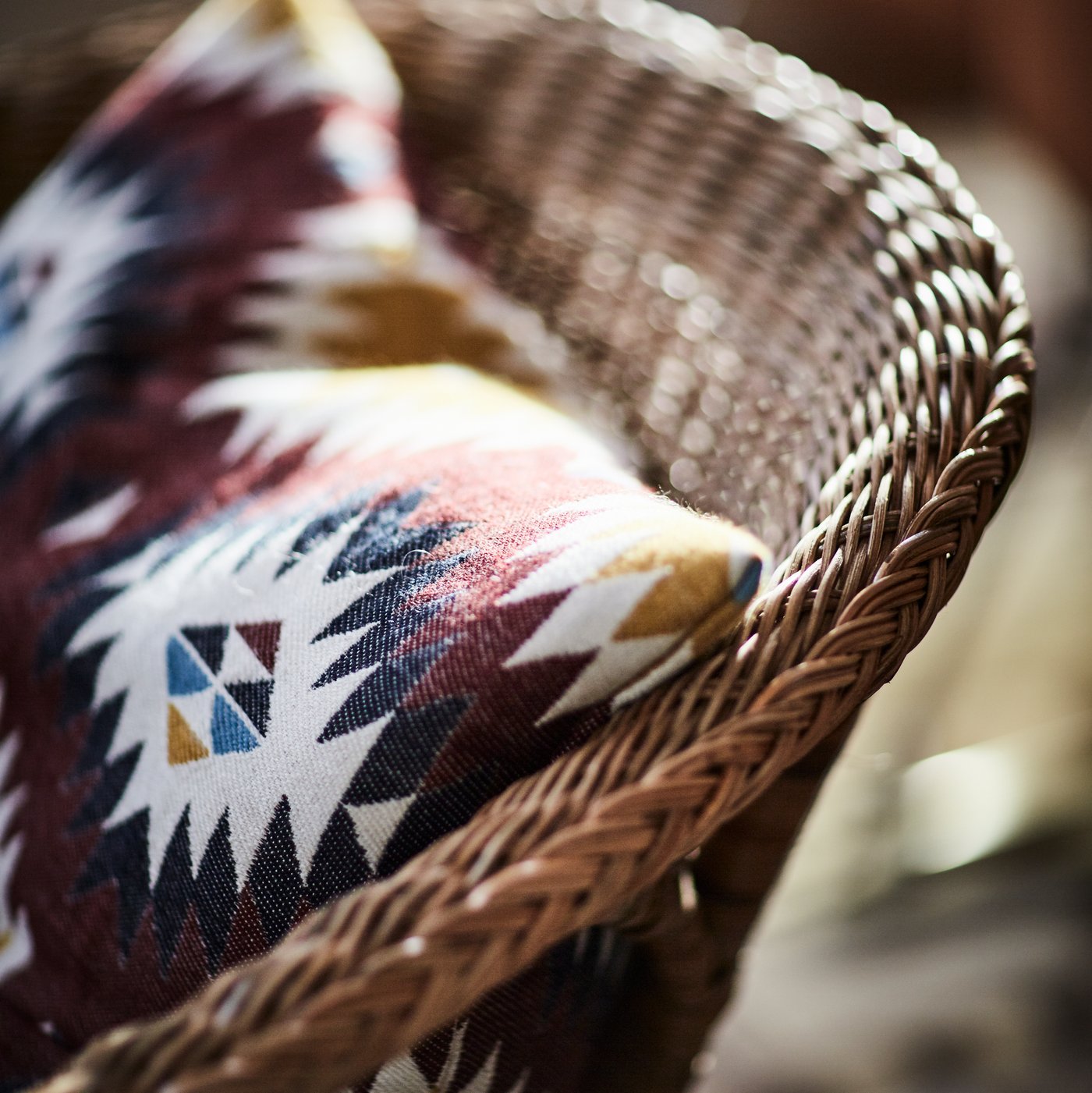 An AGEN armchair in rattan and bamboo with a cushion resting in its seat.