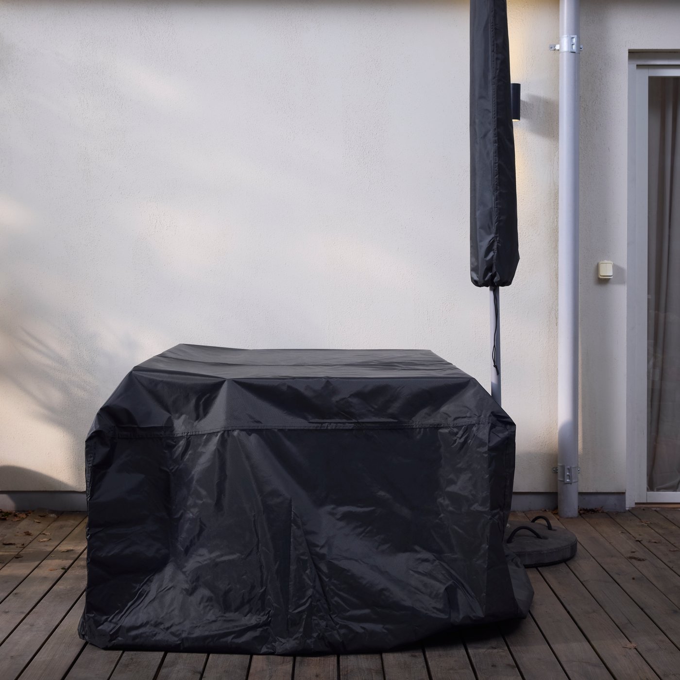 A TOSTERÖ cover for furniture set covers a piece of furniture next to a parasol covered by a TOSTERÖ parasol cover.