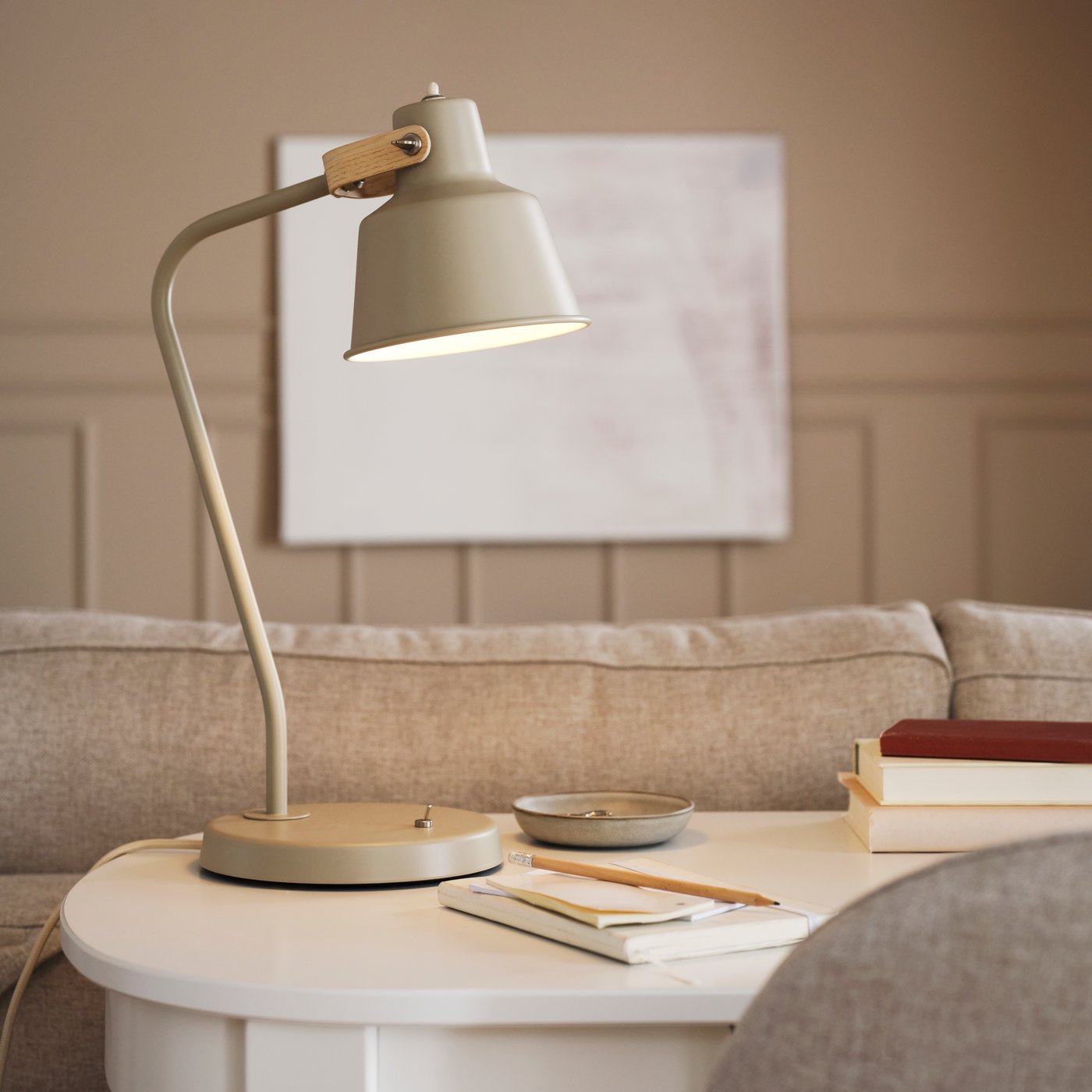 Auf einem weissen ROSENTORP Schreibtisch steht eine SJÖMAKT Schreibtischleuchte in Beige/Esche. Daneben liegen ein Bleistift und ein Notizbuch.