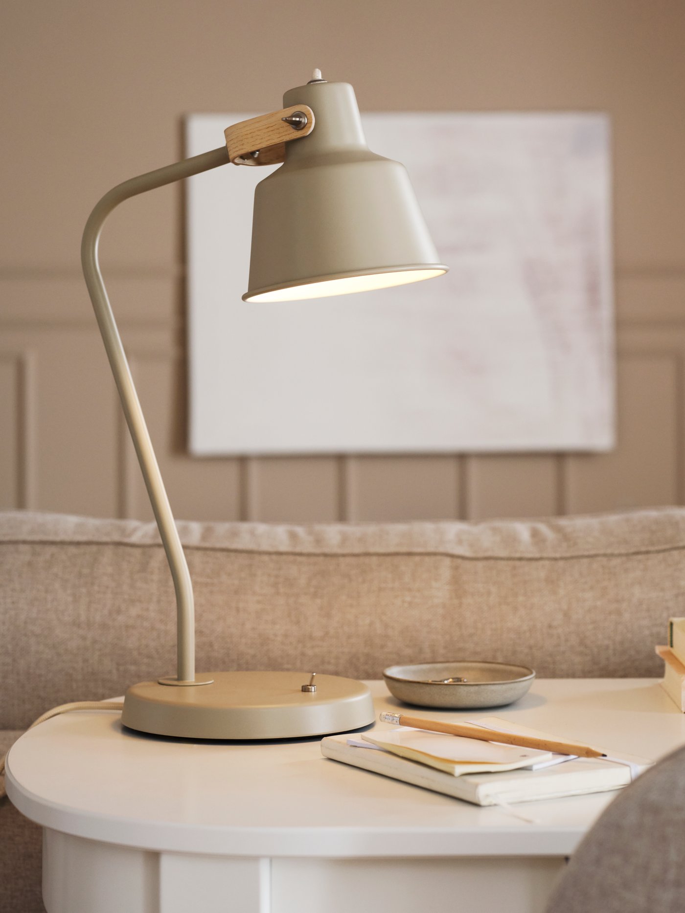 Beżowa lampa biurkowa SJÖMAKT stojąca na białym biurku.